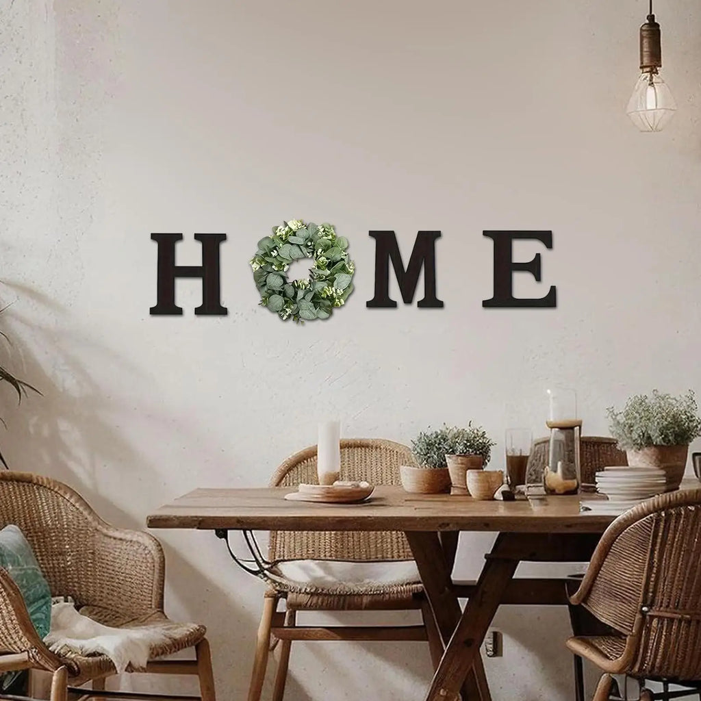 Rustic black "HOME" wooden wall letters with a green artificial eucalyptus wreath replacing the letter O.