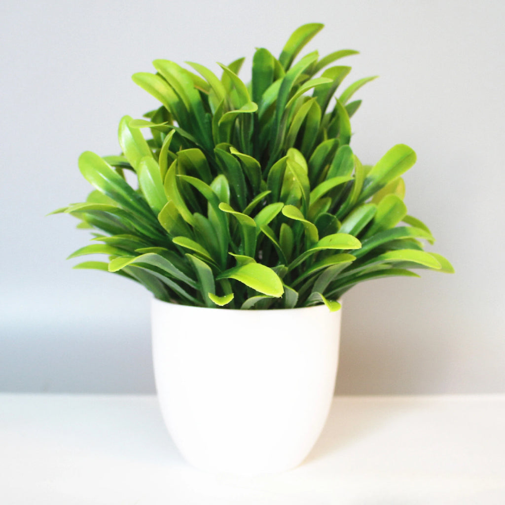 Artificial plant with vibrant, pointed green leaves in a simple, minimalist white rounded pot on a white surface.