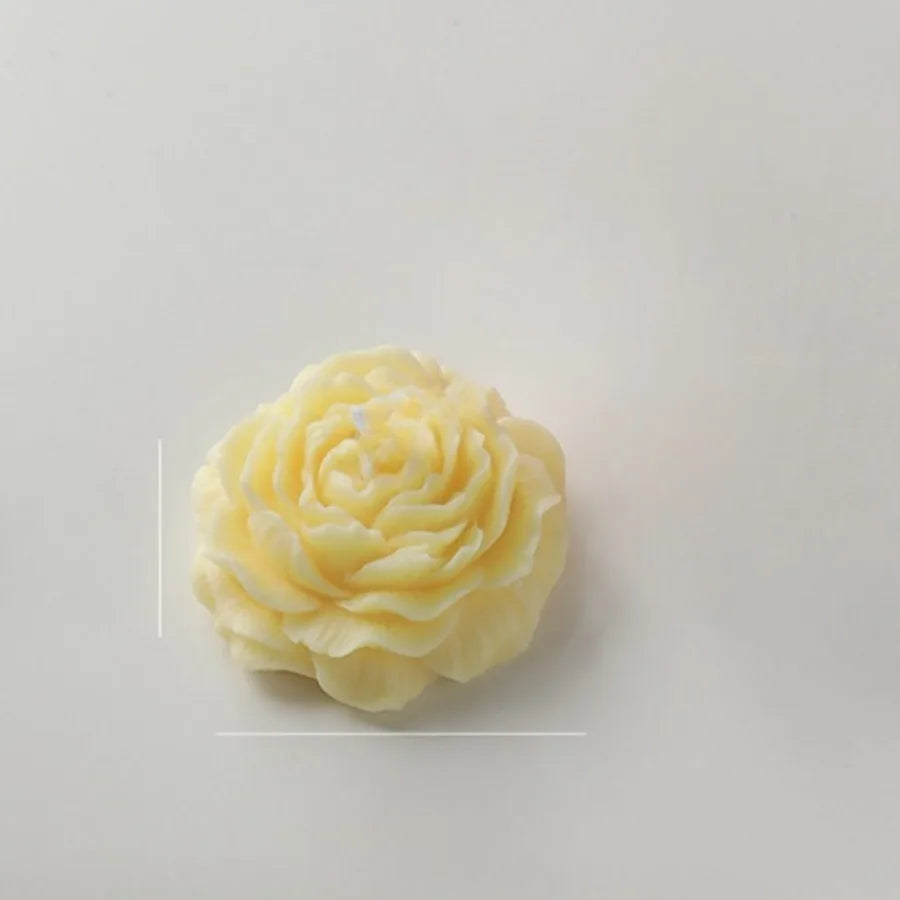 Pale yellow candle shaped like a detailed, layered rose flower, isolated on a plain background.