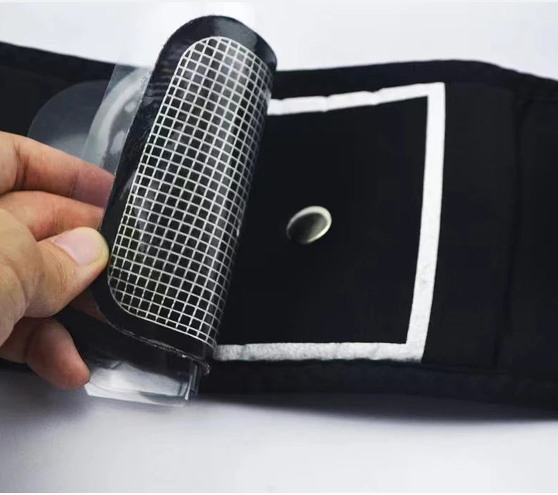 A hand peeling a clear, grid-patterned protective film from a black abdominal muscle stimulator fitness belt.