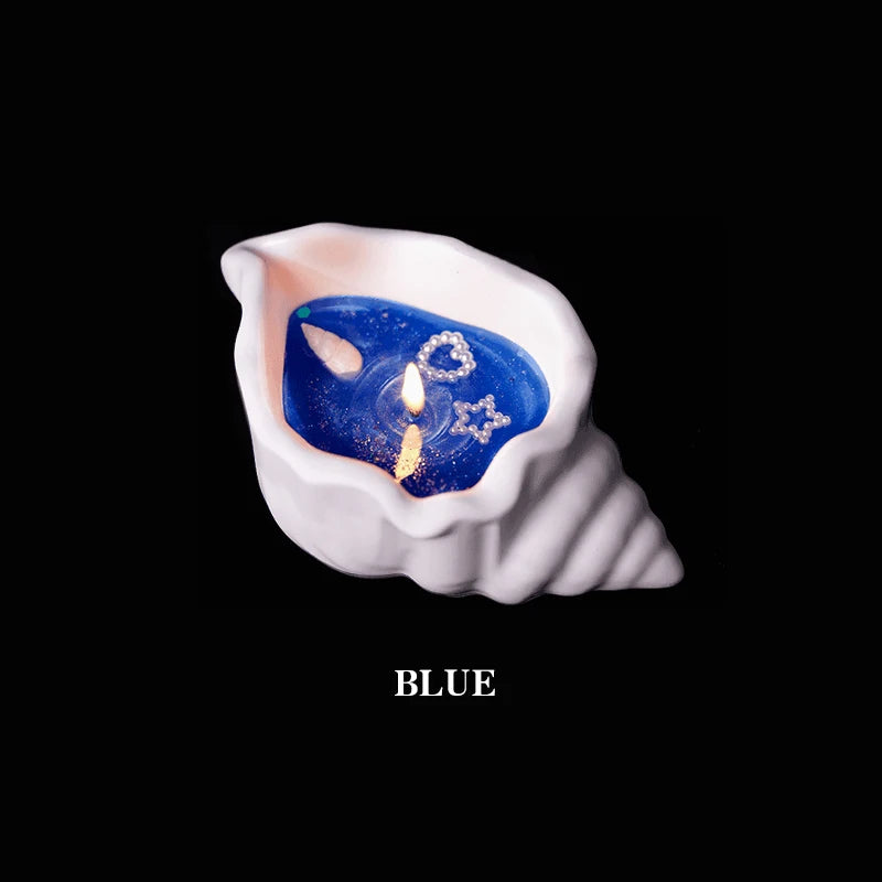 Lit blue candle in a white shell-shaped holder with decorative heart and star accents, isolated on black.