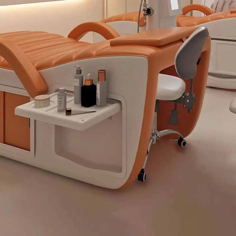 Orange and white professional massage bed featuring a side storage shelf, built-in cabinet, and matching salon stool.