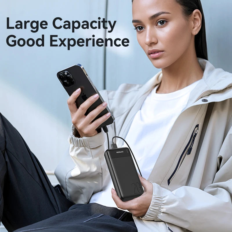 A person holding a sleek, black 20,000mAh portable power bank with an LED indicator, charging a smartphone via cable.