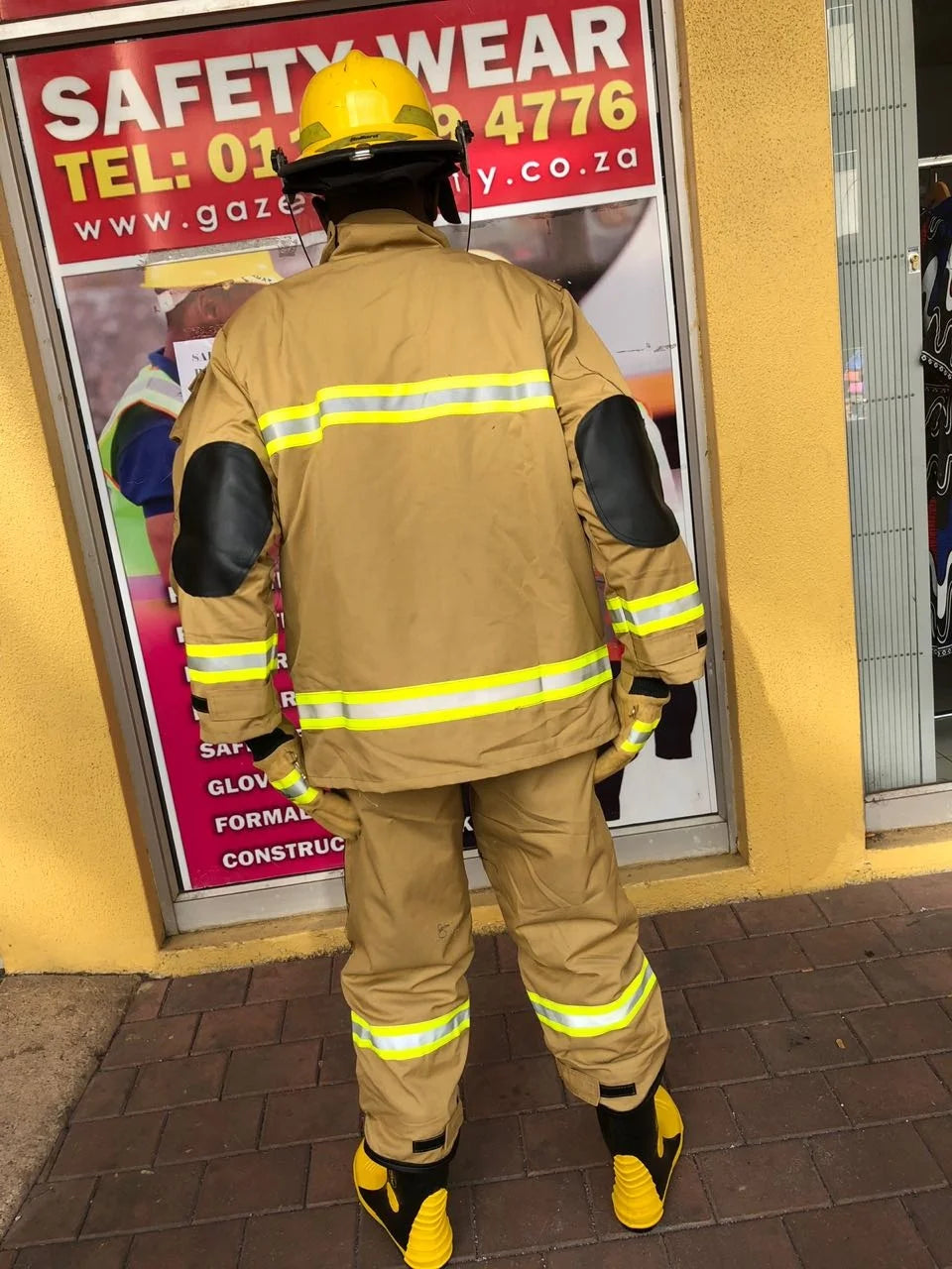 Tan firefighter gear, helmet, black elbow pads, and yellow reflective stripes on jacket and pants.