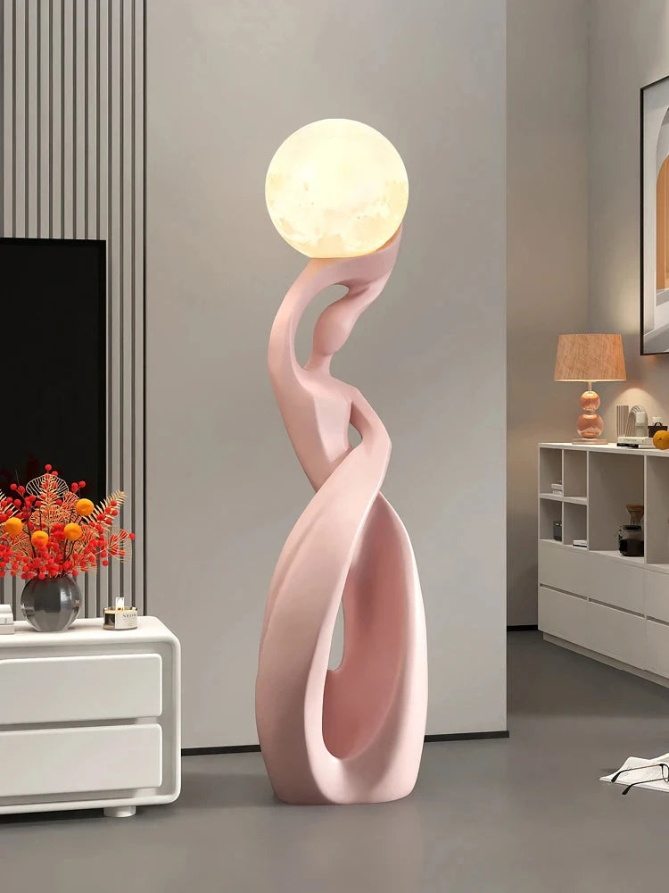 Abstract pink resin floor ornament featuring a stylised figure holding a glowing, moon-like illuminated orb.