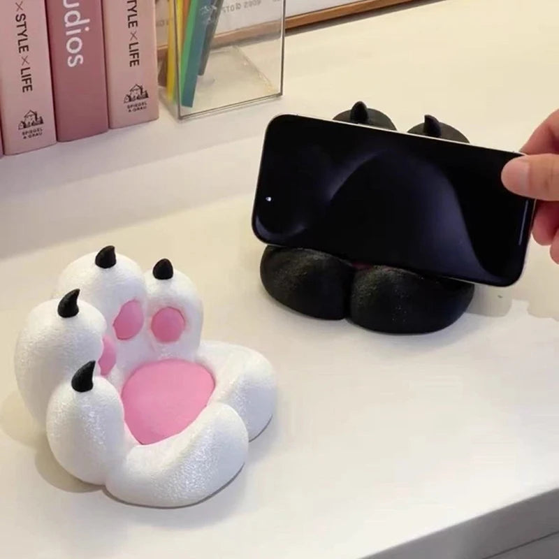 Cute cat paw-shaped phone stands in black and white, featuring pink pads and black claws, holding a smartphone.