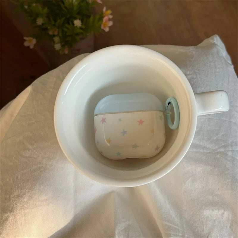 Cream AirPods case with pastel star pattern, smooth glossy finish, and light blue side ring. Fits standard AirPods.