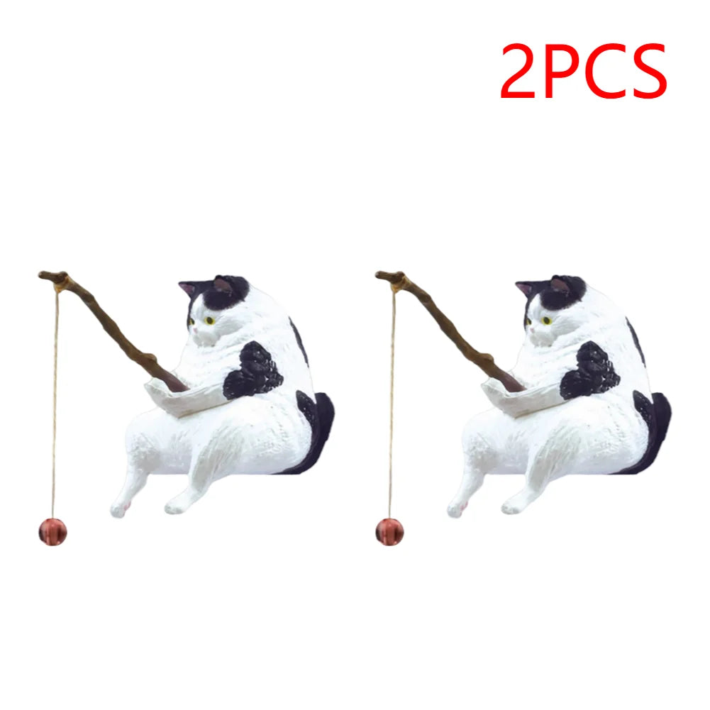 Two black and white cat ornaments, each sitting and holding a fishing rod with a hanging bauble.