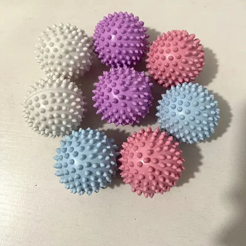 A collection of seven spiky massage balls in pastel shades of white, purple, pink, and blue.