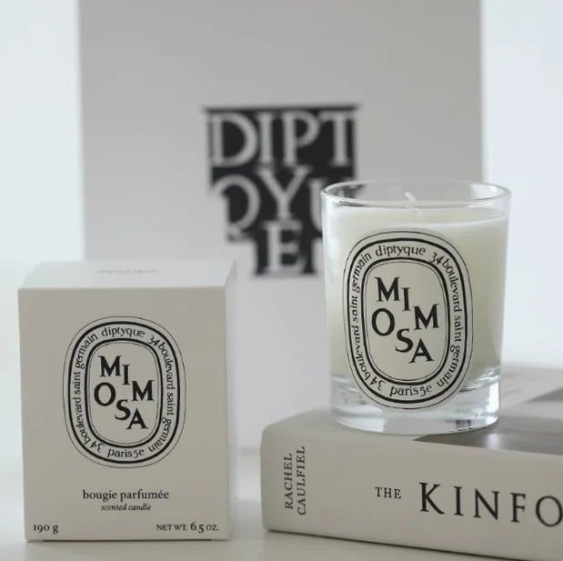 Mimosa scented candle in a clear glass jar with an oval label, shown next to its matching white product box.