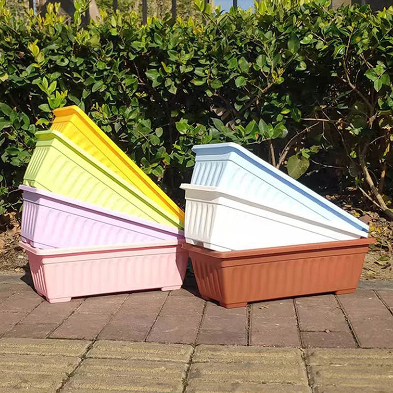 Stacked, rectangular plastic planters in various pastel and bright colors, set on a brick patio against a hedge.