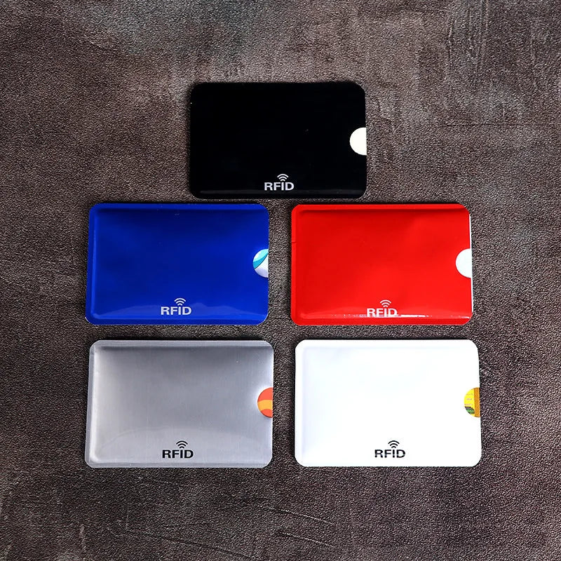 Five colored plastic RFID blocking card sleeves with thumb cutouts, arranged on a textured dark surface.