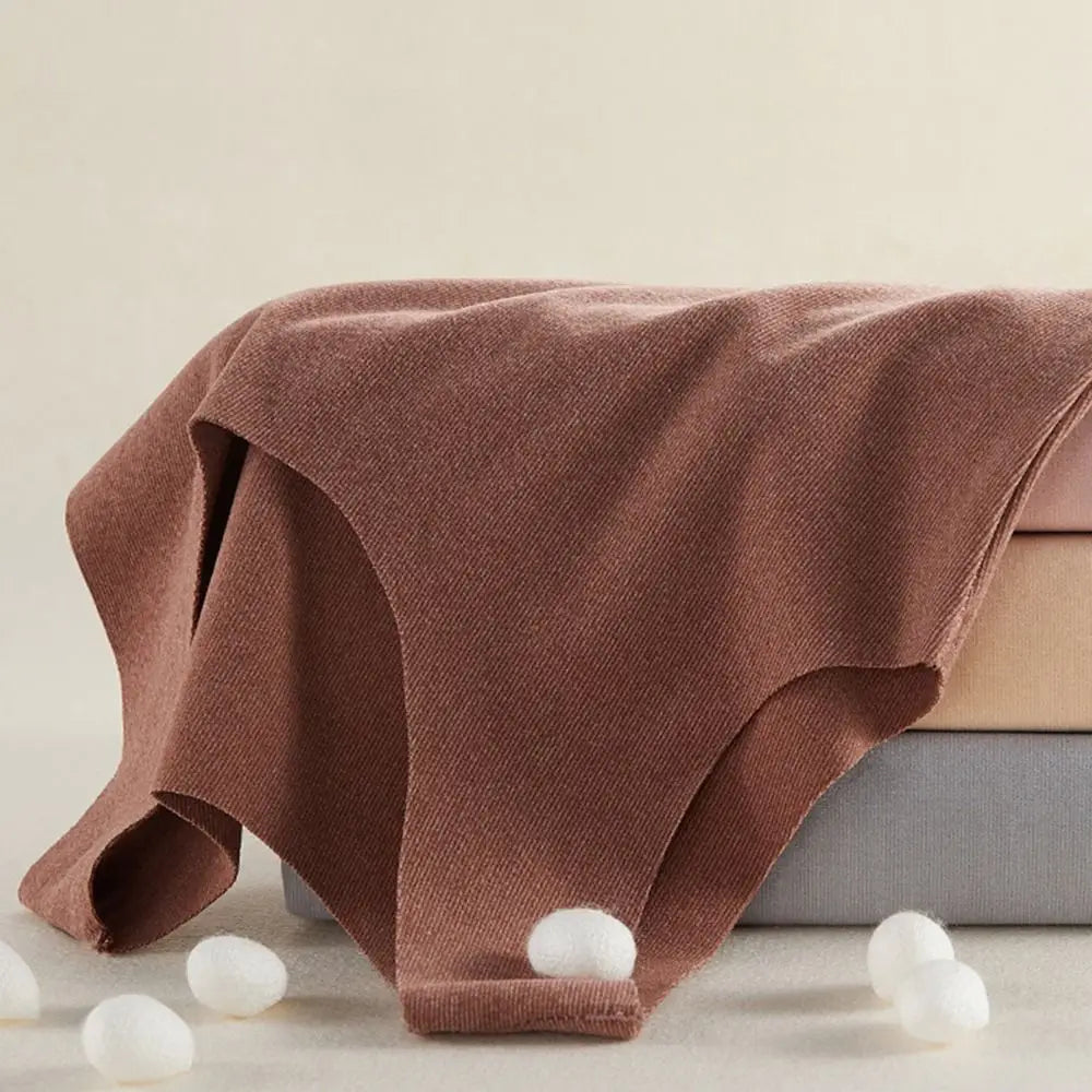Stack of seamless women's briefs in chocolate, beige, and grey shades, accented with white silkworm cocoons.