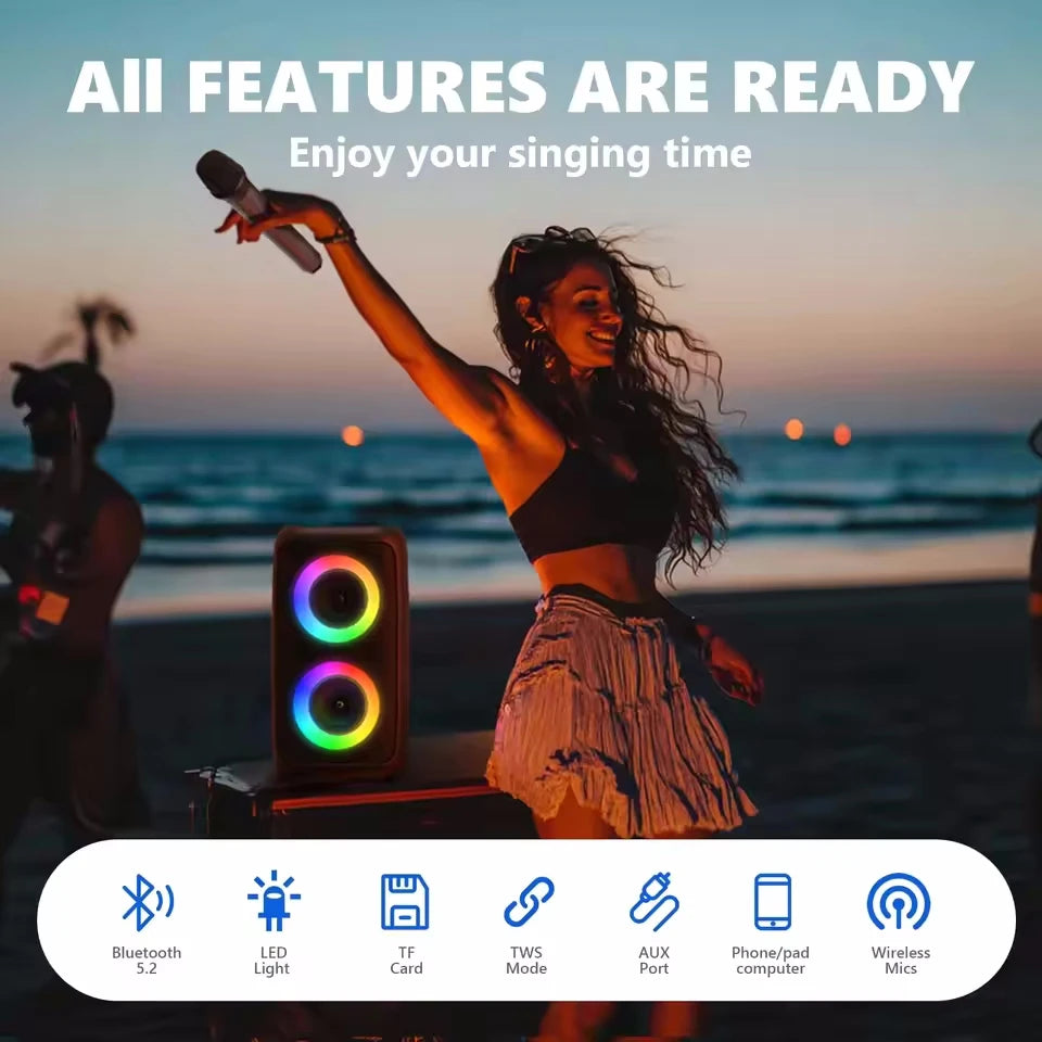 Portable black Bluetooth karaoke speaker with colourful LED light rings, seen on a beach at sunset.