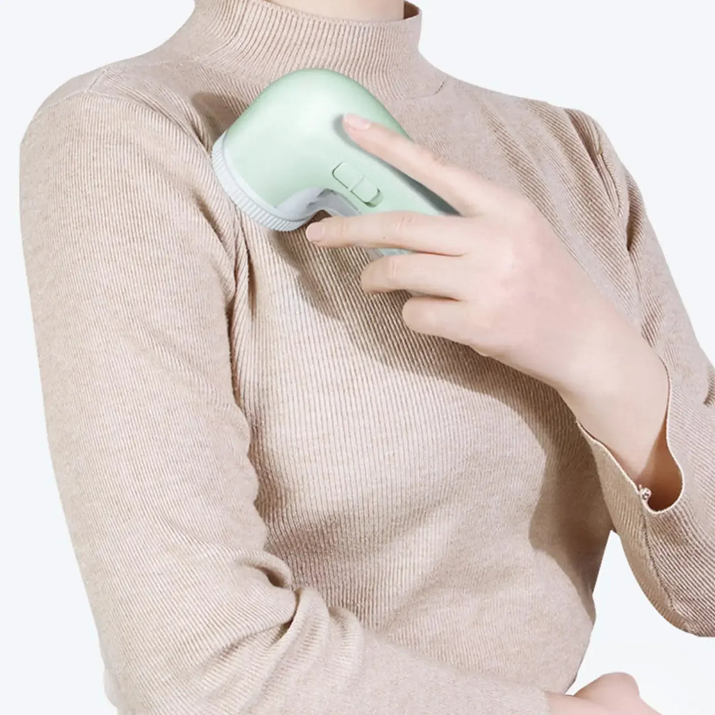 A person using a mint green, ergonomic fabric shaver on a beige ribbed jumper.