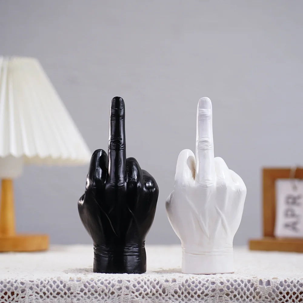 Black and white middle finger hand gesture ornaments standing on a white lacy table surface.