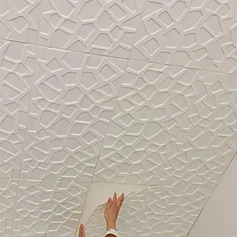 White 3D self-adhesive wall tiles with a geometric, lattice-style pattern being applied to a wall by hand.