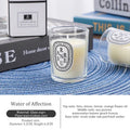 Small scented candle in a glass votive with a minimalist white oval label, resting on a blue woven placemat.