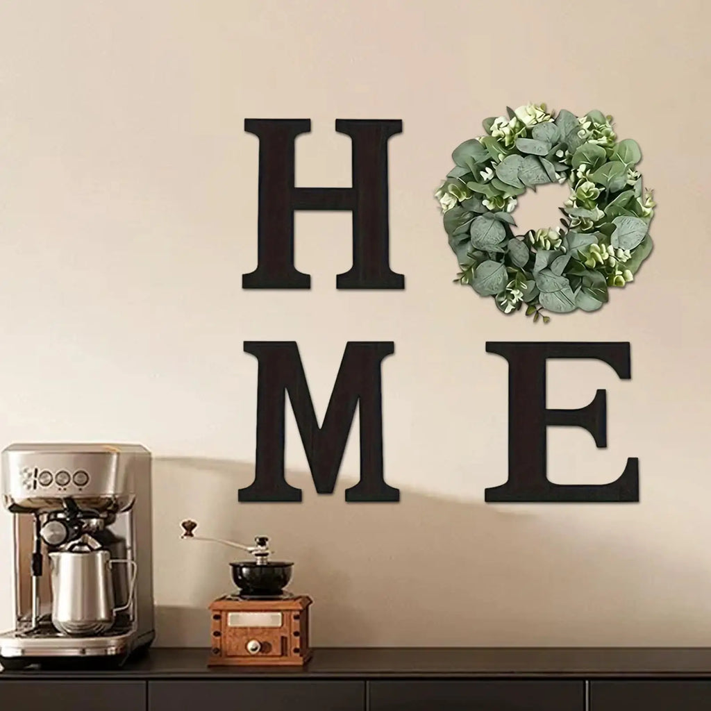 Rustic black wooden 'HOME' wall sign with an artificial eucalyptus wreath replacing the 'O'.