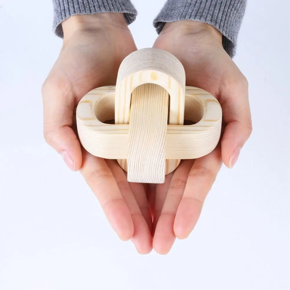 Two hands holding a minimalist, interlocking natural wood sculpture with smooth, rounded shapes.