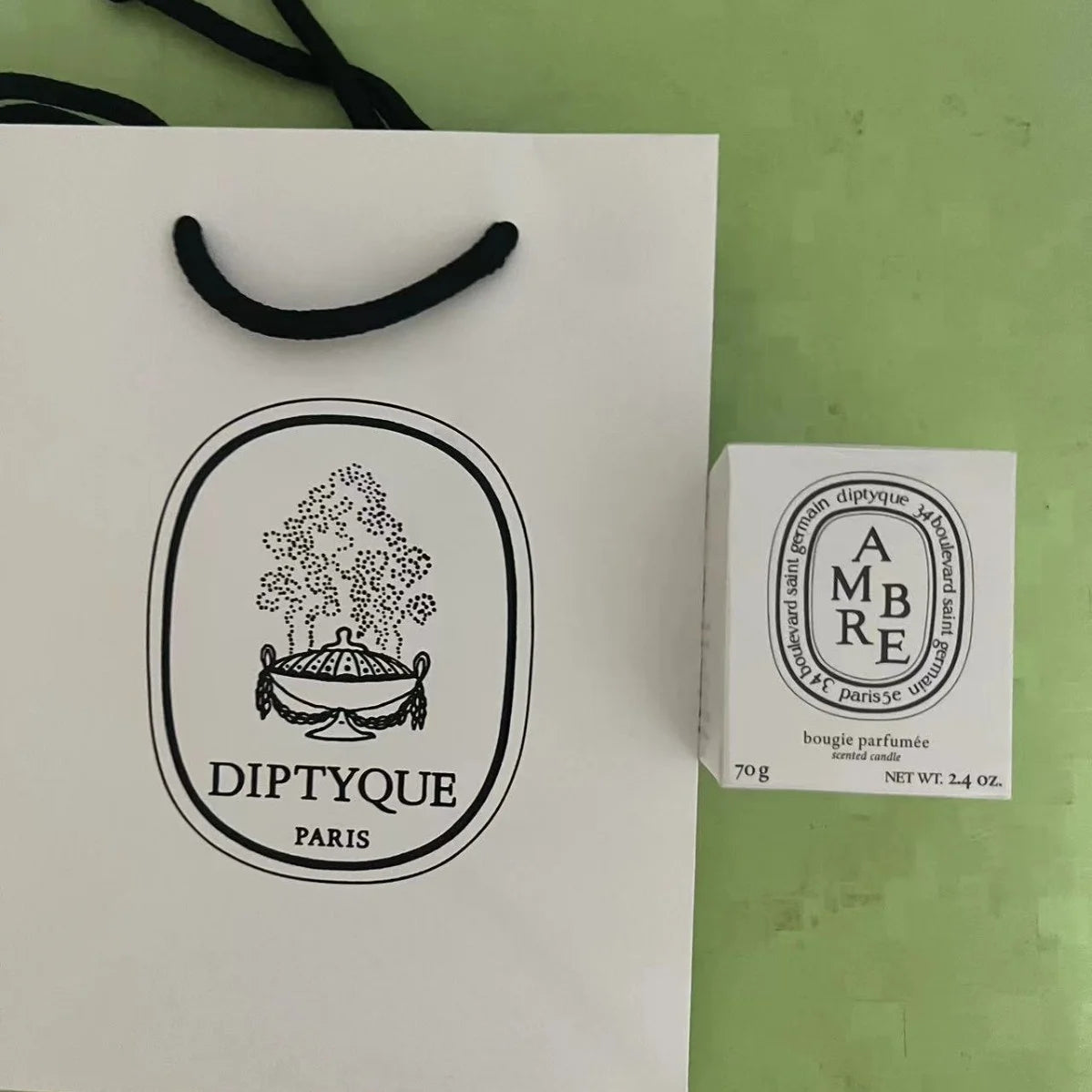A white scented candle box and matching paper carrier bag, both featuring elegant black graphic designs.