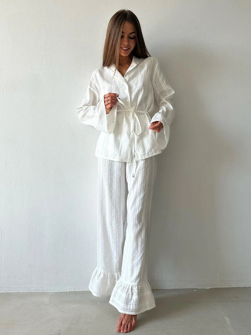 Woman wearing white textured pajama set with a button-up tie-waist shirt and wide-leg trousers with ruffled hems.