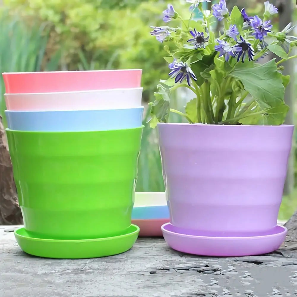 A stack of colorful, ribbed plastic pots and a lavender pot holding a flowering plant, all with matching base trays.