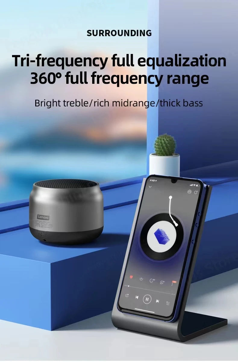Compact, cylindrical silver Bluetooth speaker with a sleek metallic finish, sitting next to a smartphone on a stand.