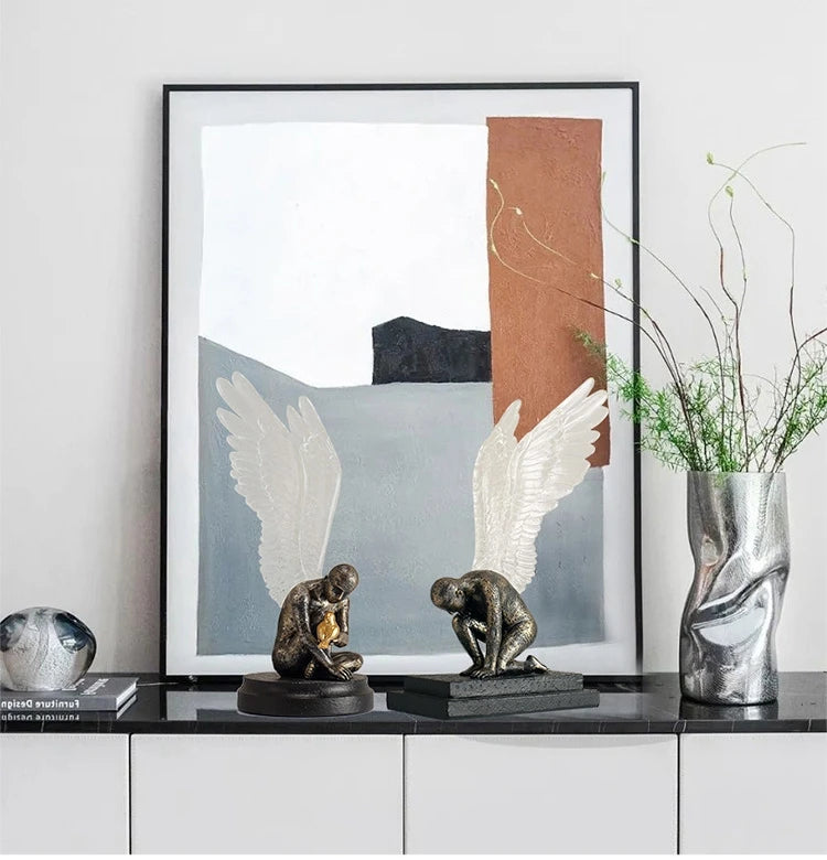 Two bronze-effect kneeling angel sculptures with white textured wings displayed on a shelf.