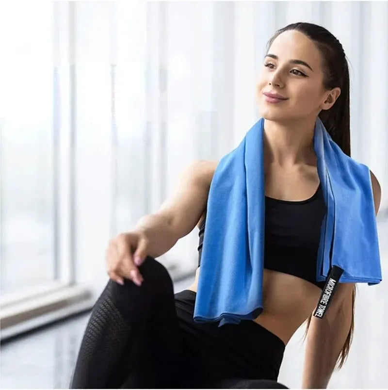 A woman in gym wear with a bright blue microfibre towel draped over her neck in a bright fitness studio.
