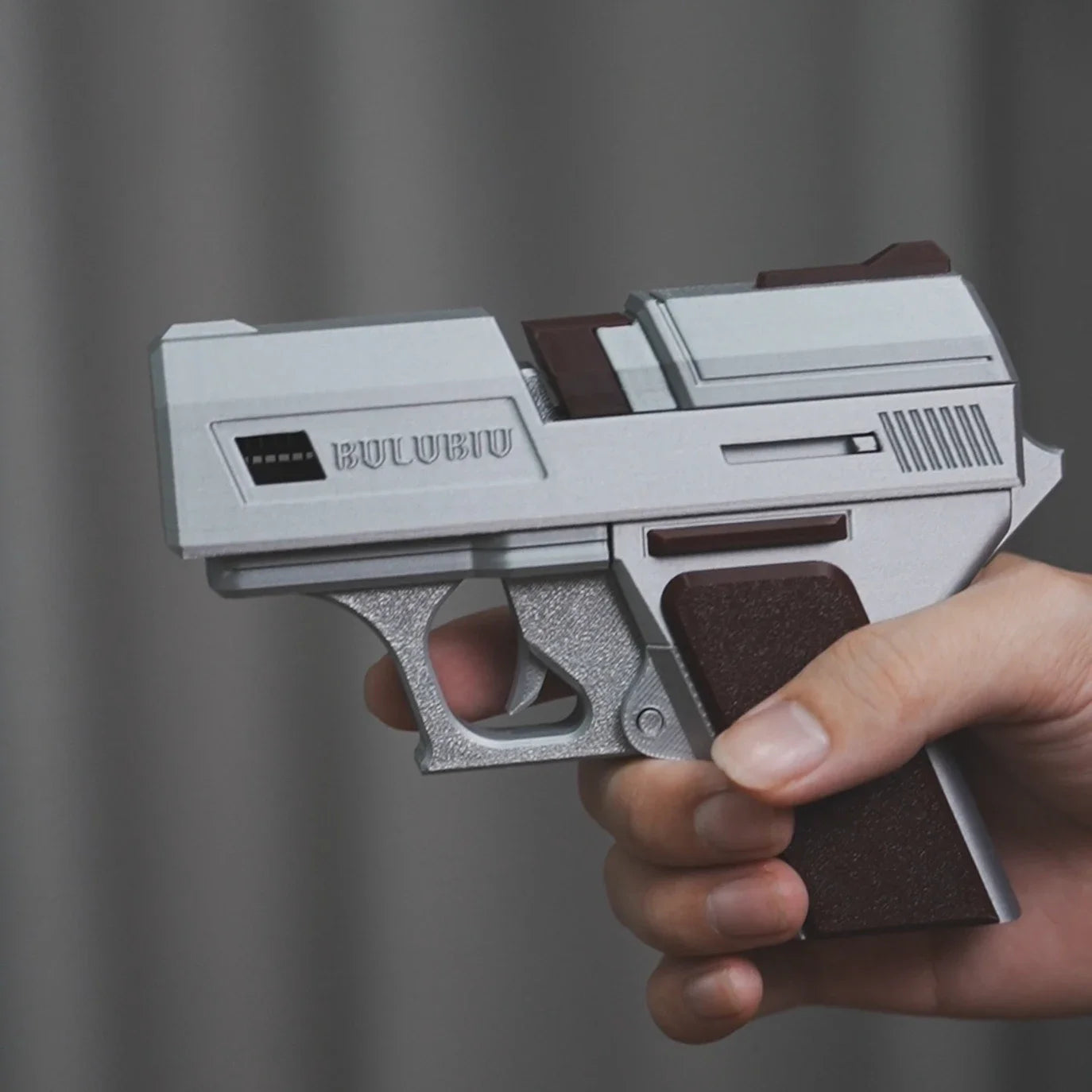 Silver and dark brown pistol-style AirPods case with matte plastic finish, held in a hand.