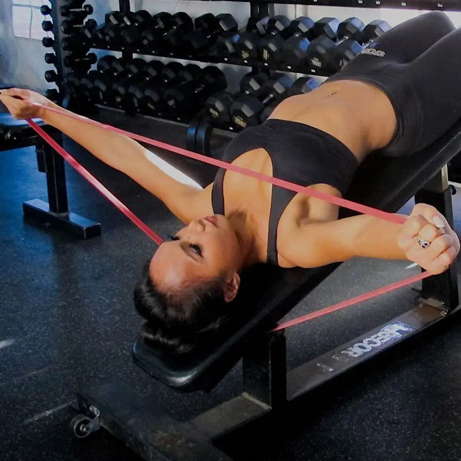 A woman lying on a gym bench using a flat, red heavy-duty resistance band for chest exercises.