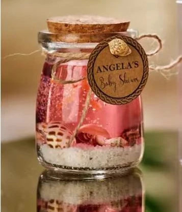 Small glass jar with pink liquid, white sand, and seashells, finished with a cork stopper and personalised gift tag.