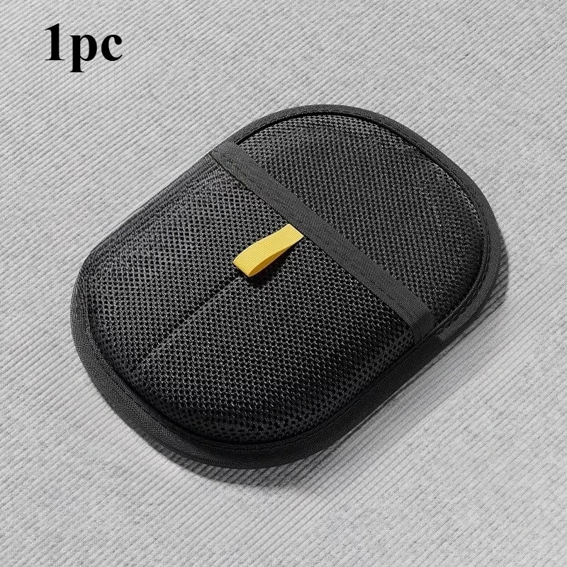 Oval black mesh exfoliating sponge with a yellow finger strap, set against a grey textured background.