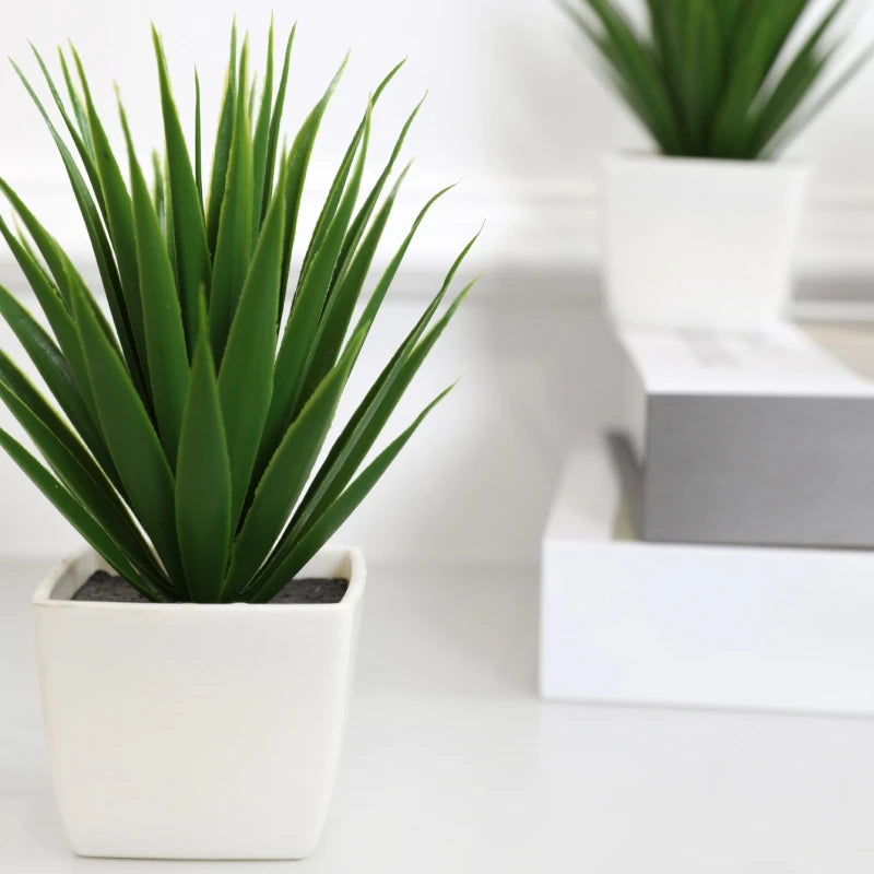 A vibrant green artificial spiky plant in a small, modern white square pot, set against a bright, minimalist background.