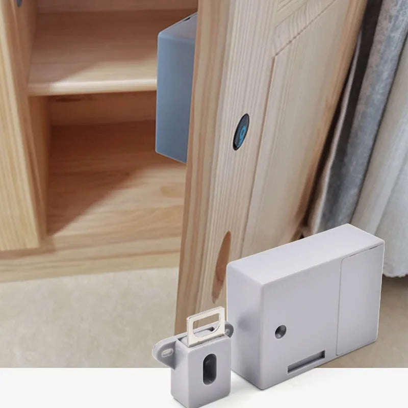 Grey plastic hidden cabinet lock with a latch mechanism, shown installed on a light wood cupboard door.