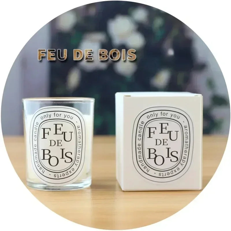 A Feu de Bois scented candle in a clear glass jar alongside its white presentation box on a wooden table.