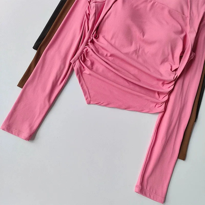Pink long-sleeved, ruched-side cropped top with a fitted, comfortable silhouette, stacked over dark brown layers.