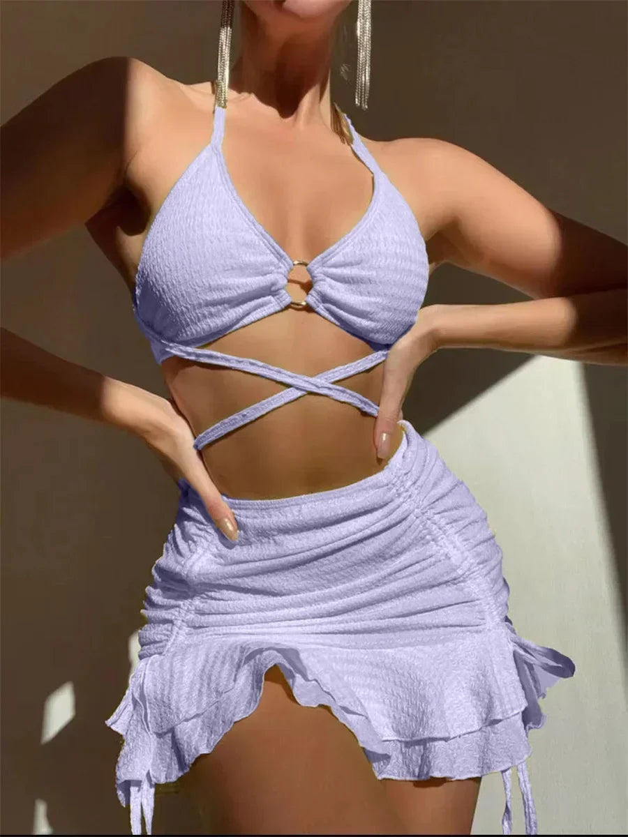 Light purple 3-piece swimsuit featuring a ring-linked halter top, criss-cross waist ties, and a ruffled skirt.