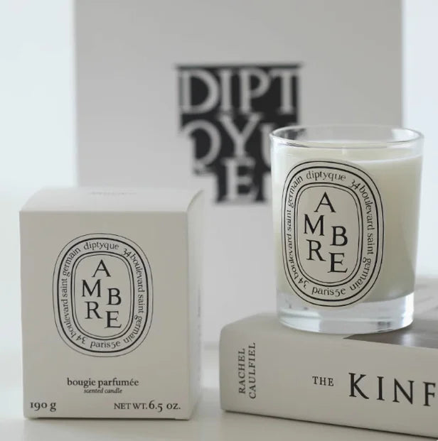Clear glass scented candle with cream wax, featuring an elegant oval white label, displayed with its matching box.