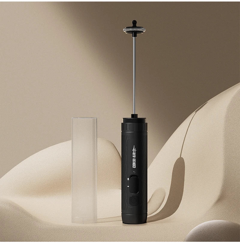 A sleek, black electric handheld milk frother with a metal wand, shown next to its clear protective cover.