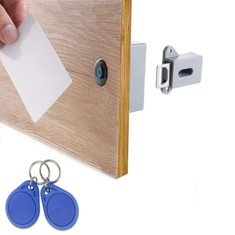 Grey plastic invisible RFID cabinet lock with two blue key fobs and a white access card on a wood cabinet door.