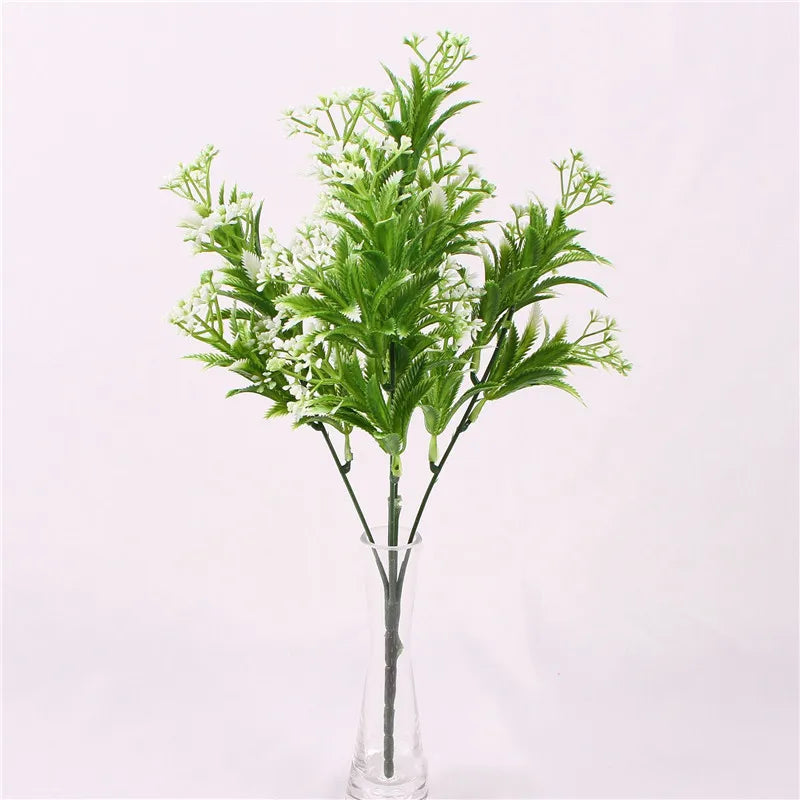 Artificial plant with feathery green leaves and clusters of small white flowers in a clear glass vase.