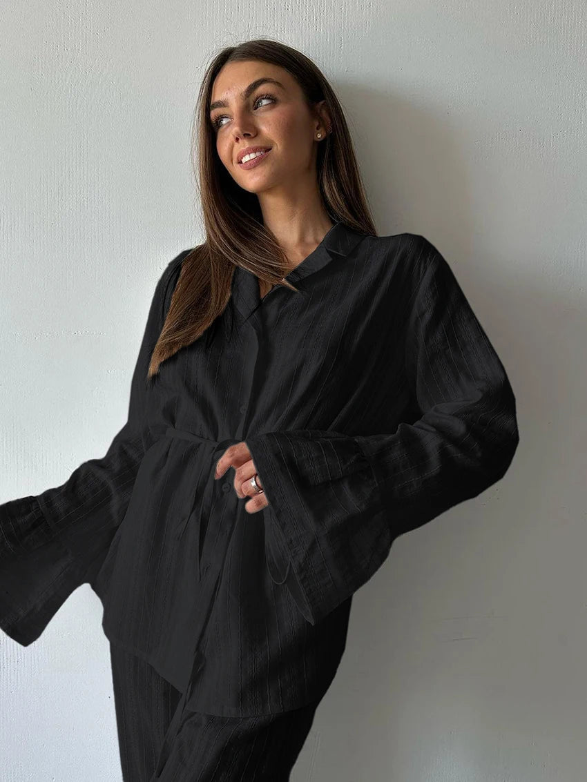 Woman wearing a black, long-sleeved button-up shirt with a belted waist and flared bell sleeves.