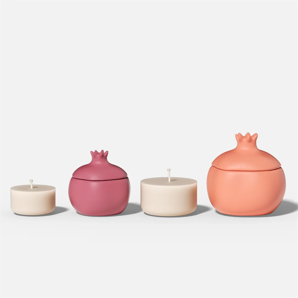 Two pomegranate-shaped candle jars in pink and peach, each with two matching refill candles with wicks.