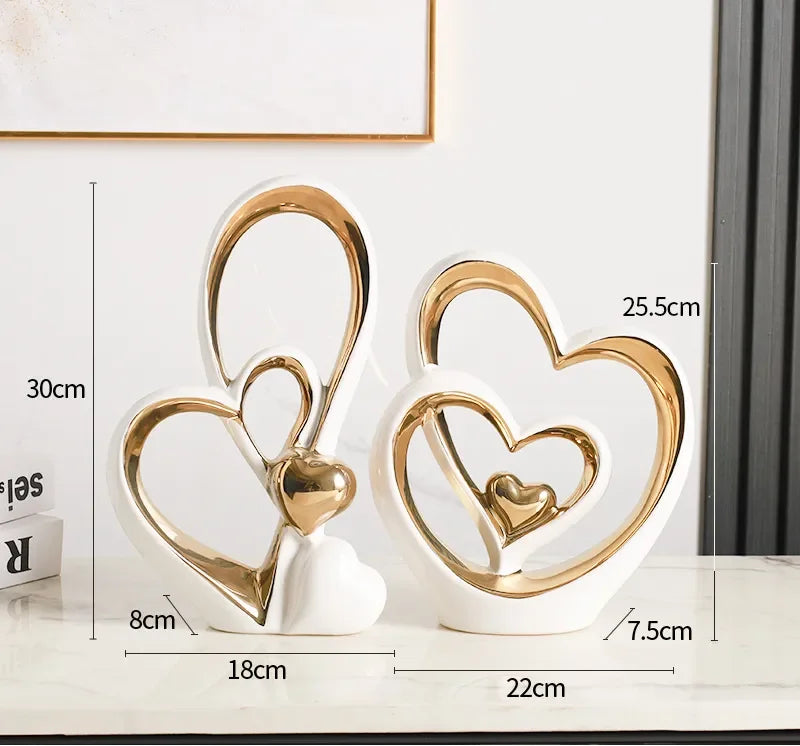 Two modern white and gold heart-shaped ceramic ornaments with openwork designs on a marble surface.