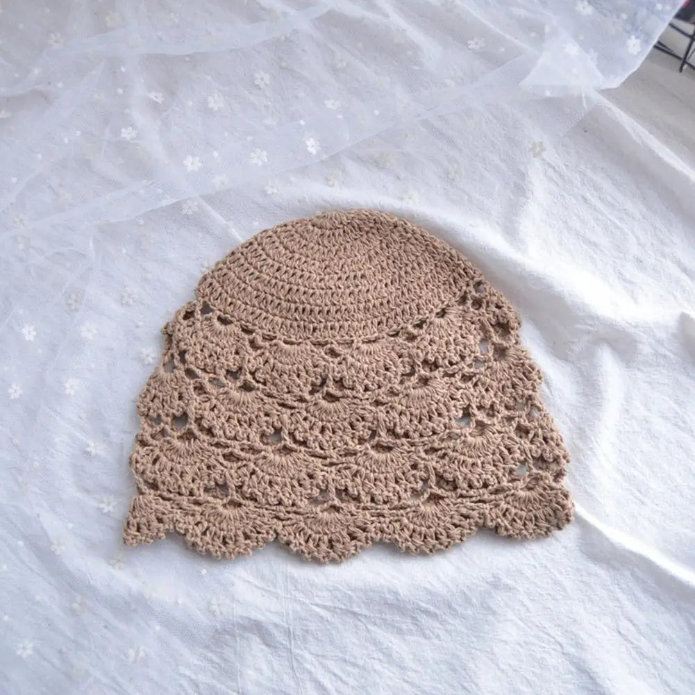 Beige crochet lace hat with a delicate, scalloped hollow pattern on a white fabric background.