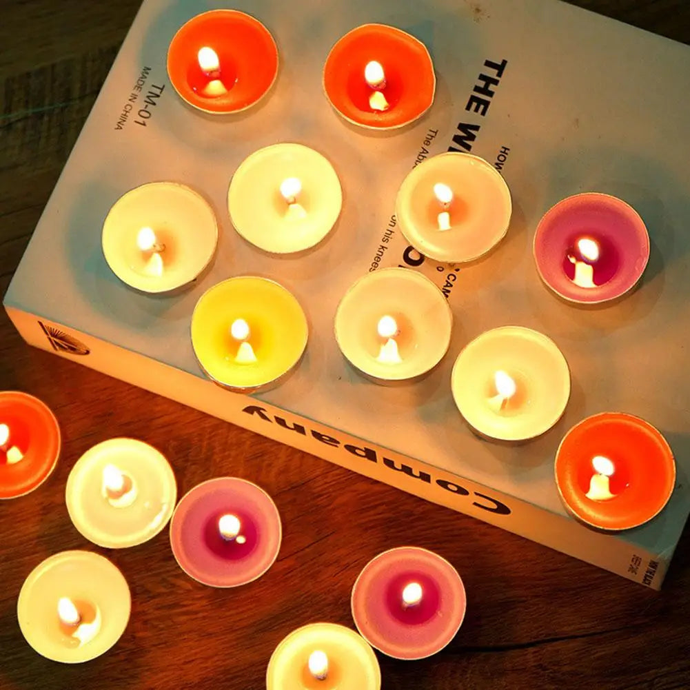 Multi-coloured lit tea light candles in metal cups, scattered on a book and wooden surface.