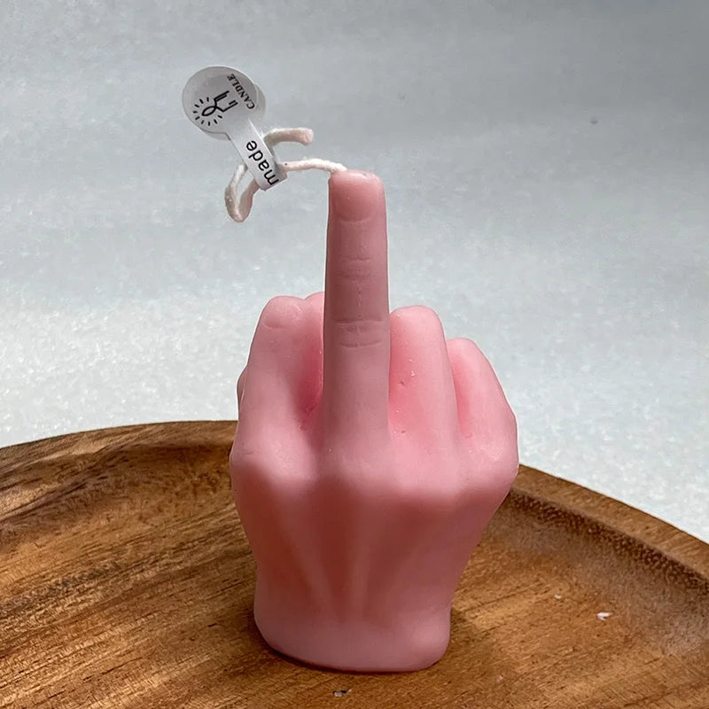 Pink candle shaped like a hand giving the middle finger, resting on a small wooden dish.