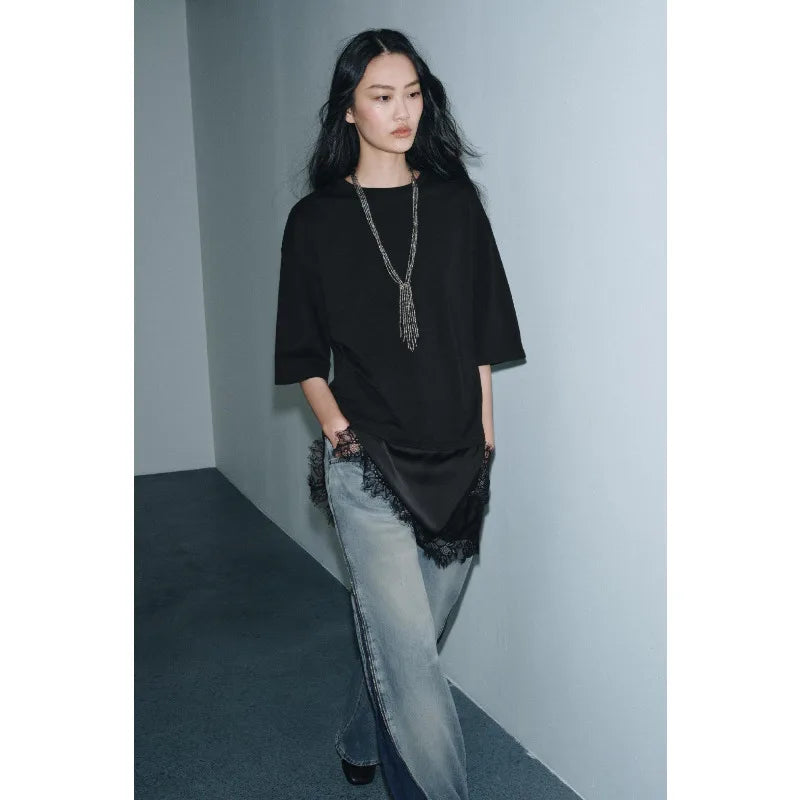 Model wearing a black oversized T-shirt with a satin hem and delicate lace trim, paired with light blue denim jeans.